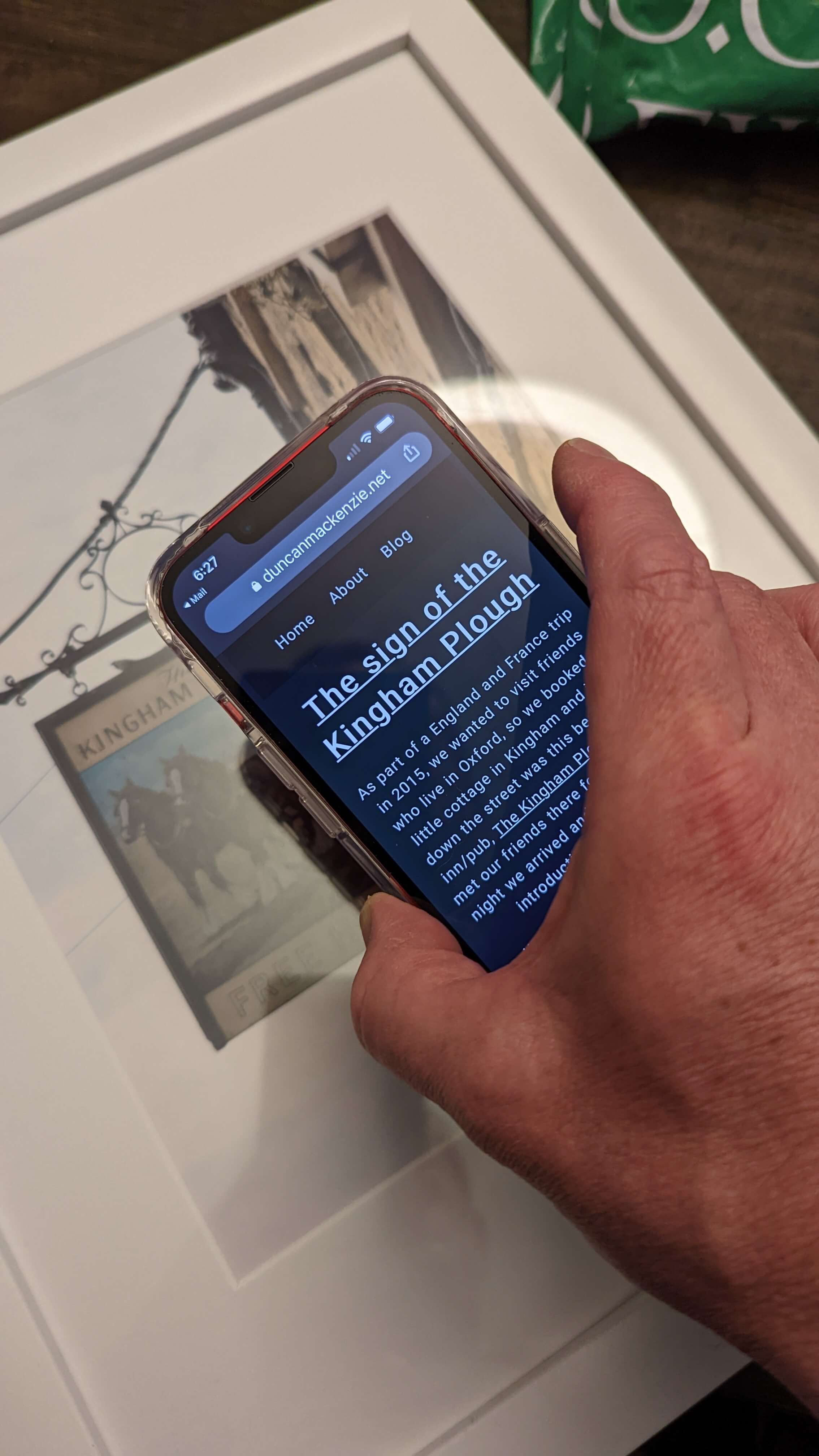 shot of an iOS phone held near the picture frame, photo info page visible on the device